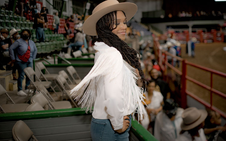 A woman wearing a white fringe jacket and twirling in a crowd of people, posing for the camera.